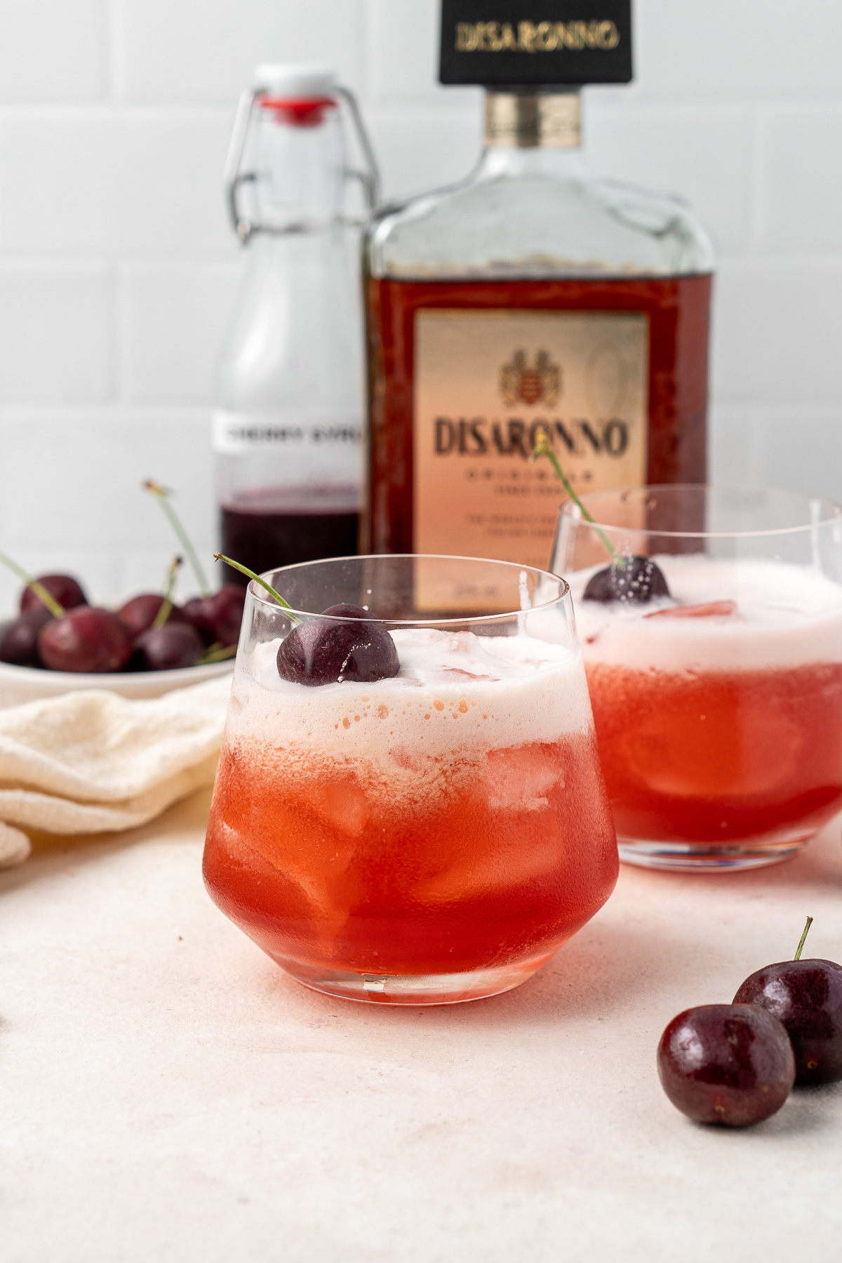 Two glasses of cherry amaretto sour garnished with fresh cherries.