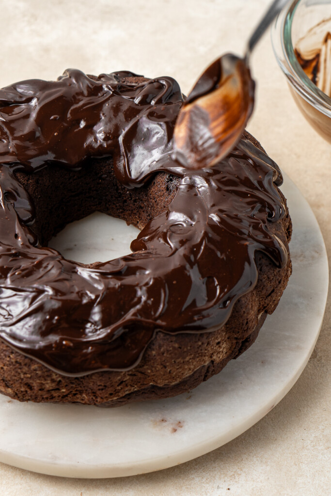 Adding the chocolate ganache to the cake with a spoon.