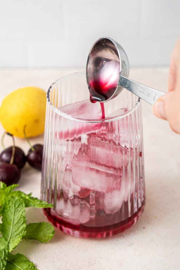 Adding cherry syrup to a glass with ice.