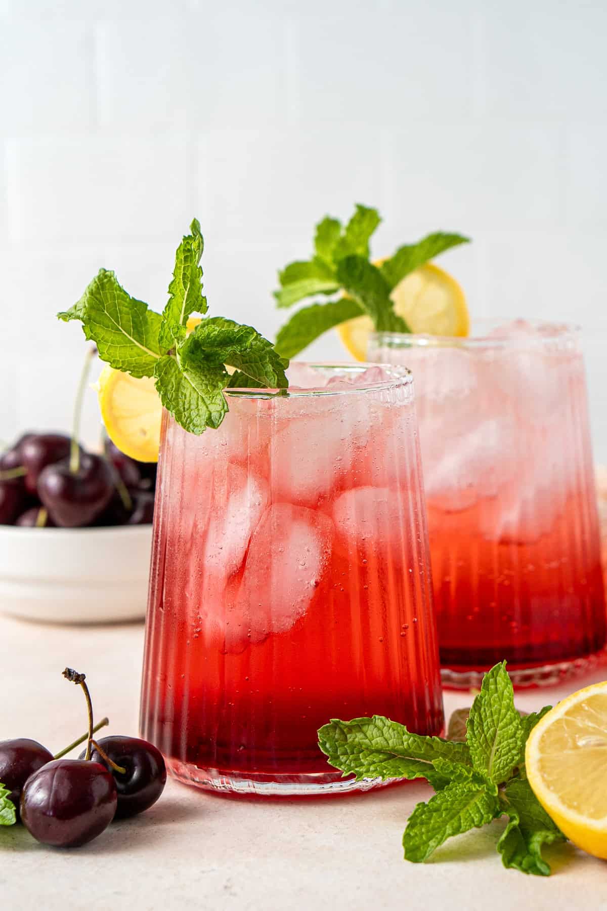 Two non alcoholic cherry spritzes with mint and lemon.