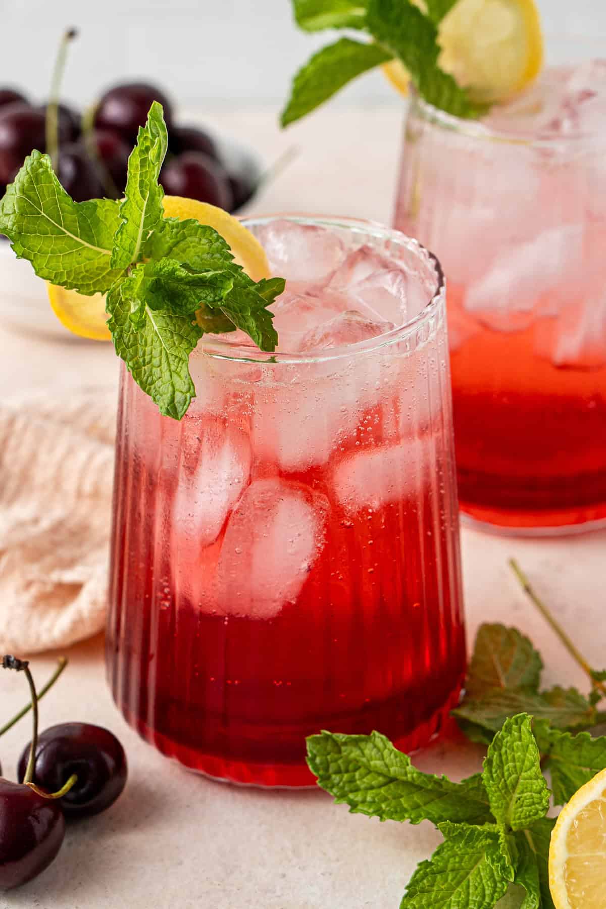 Non alcoholic cherry spritz in a glass with ice finished with fresh mint and lemon.