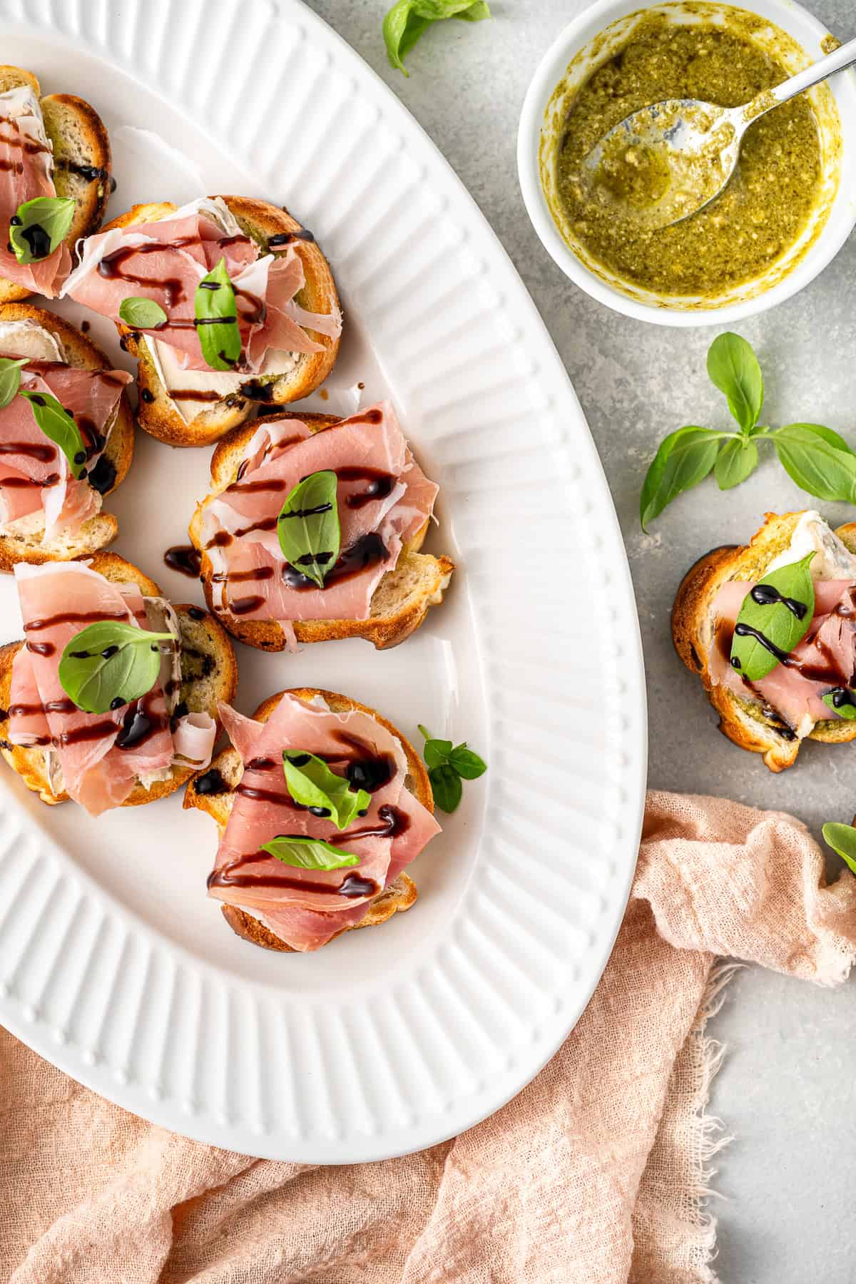 A platter of prosciutto crostini with balsamic glaze and pesto.