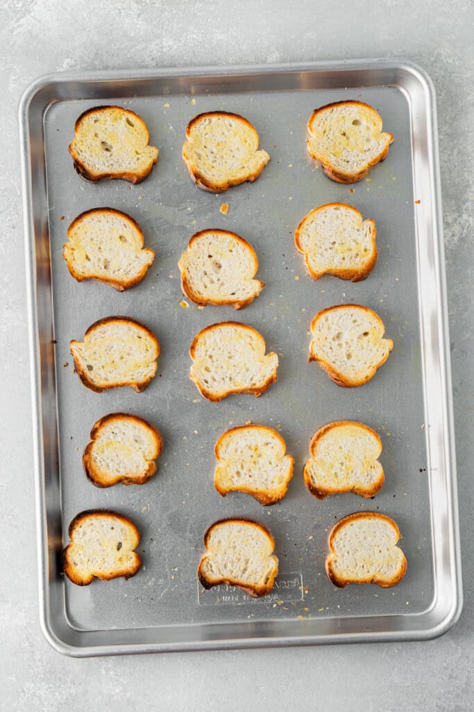 The toasted baguette sliced on a baking tray.