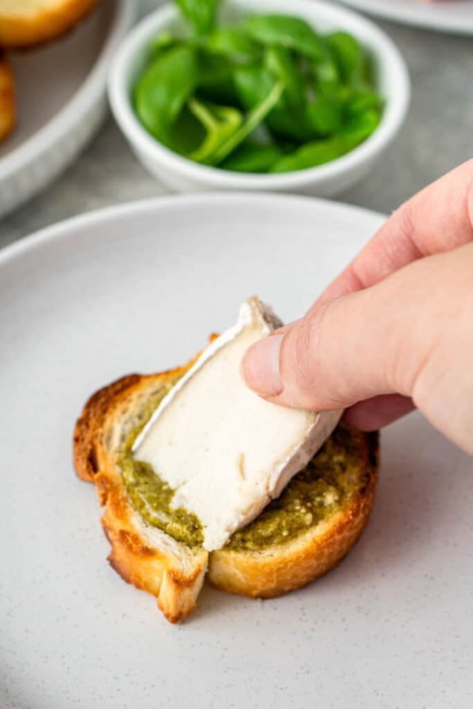 Placing a wedge of dairy free camembert onto the crostini.