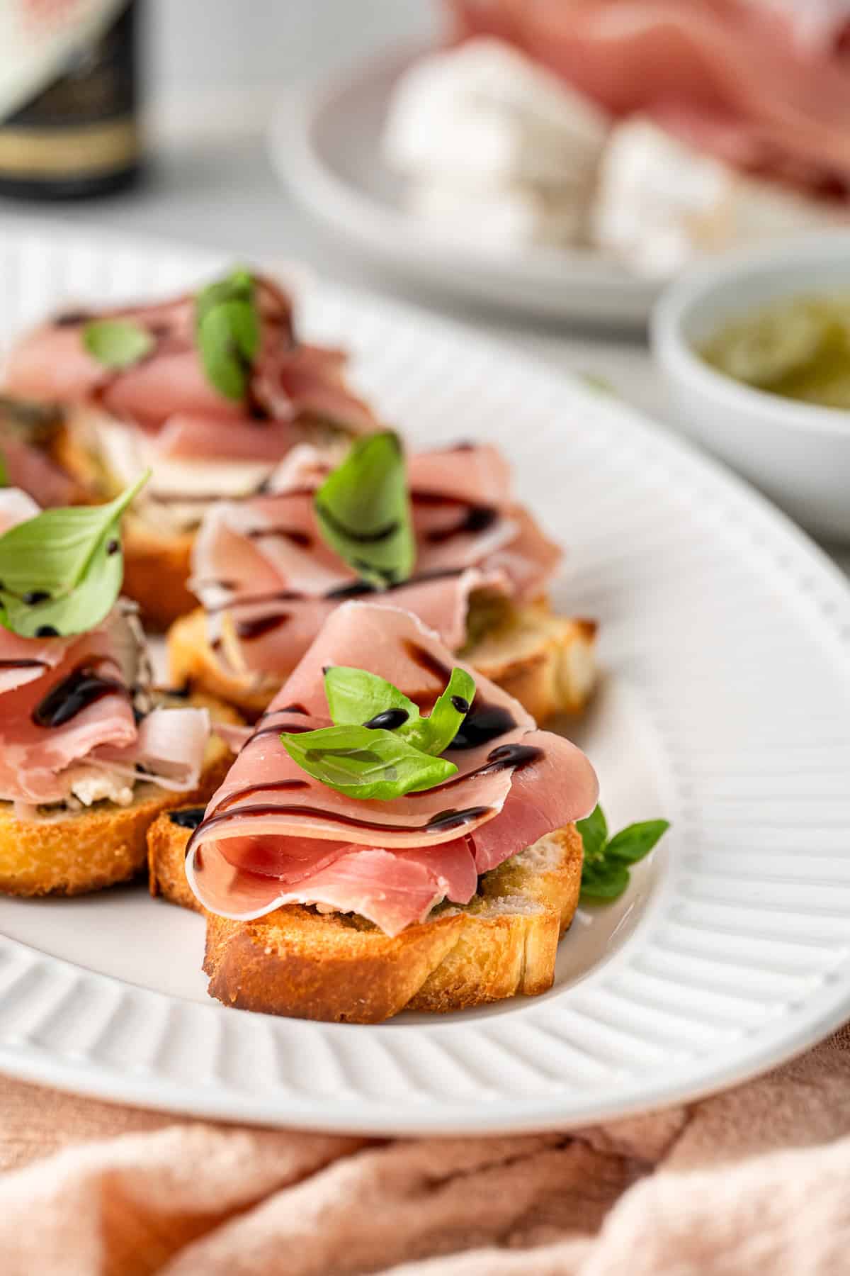 A close up of a prosciutto crostini with basil and balsamic glaze.