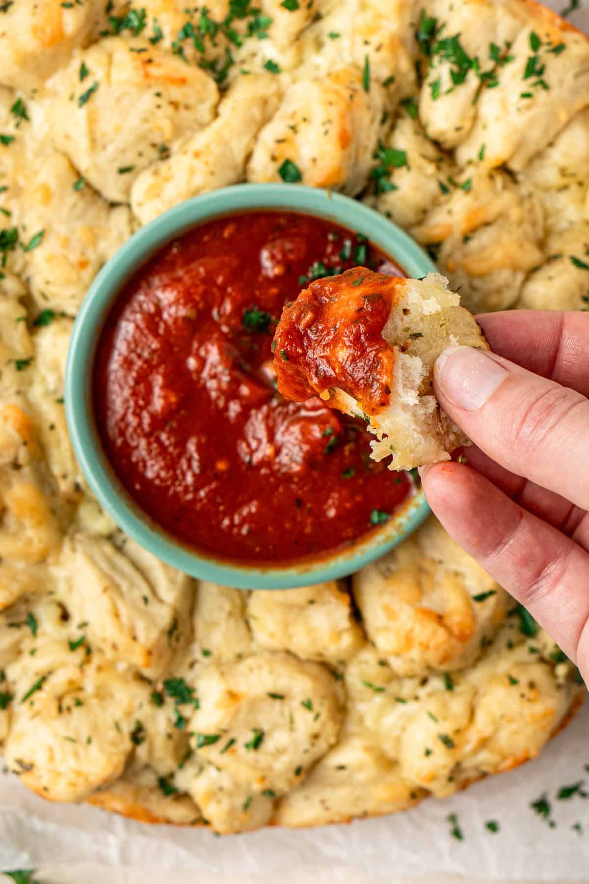 Close up of a piece of garlic bread being dunked in the marinara sauce.