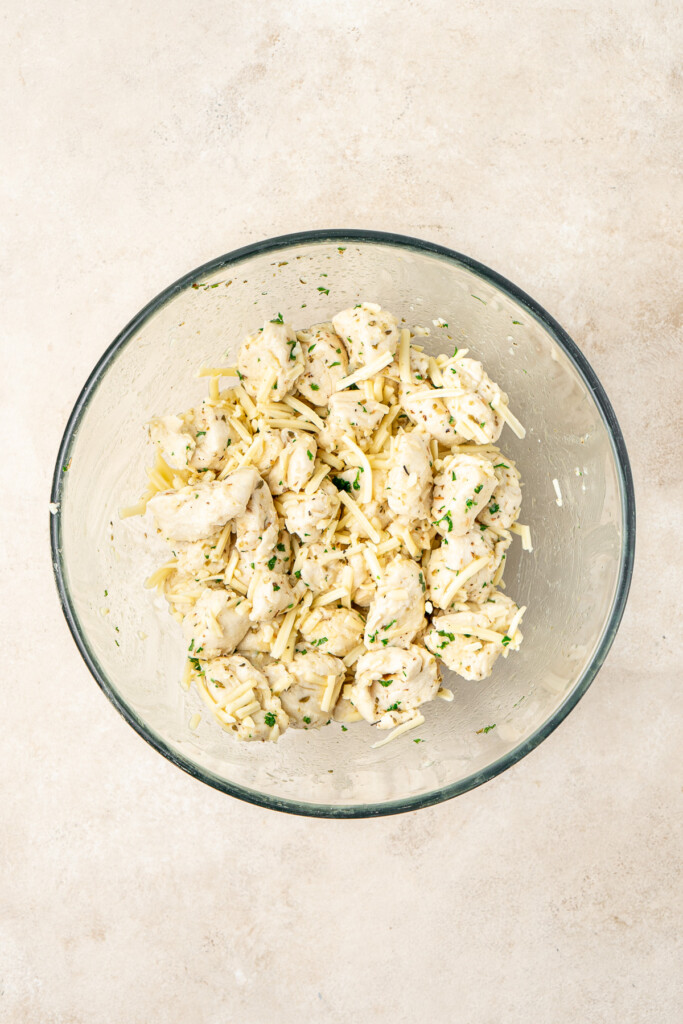 The cut up dough in a bowl with the garlic butter and cheese.