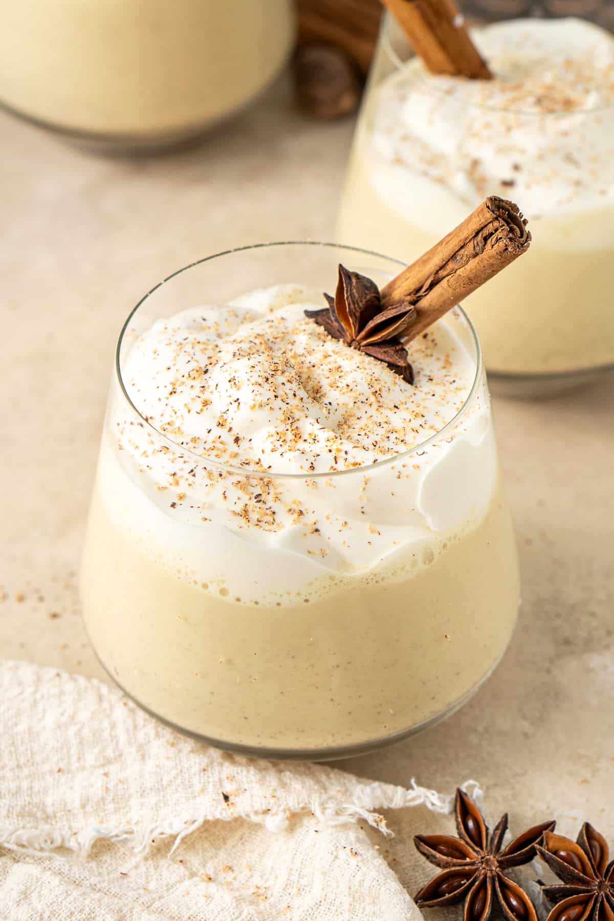 Close up of Vegan eggnog served in a glass with whipped cream and grated nutmeg and a cinnamon stick.