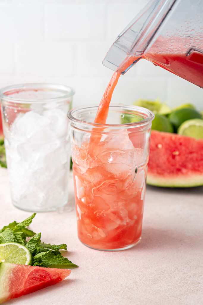 Pouring watermelon juice over ice into a glass.