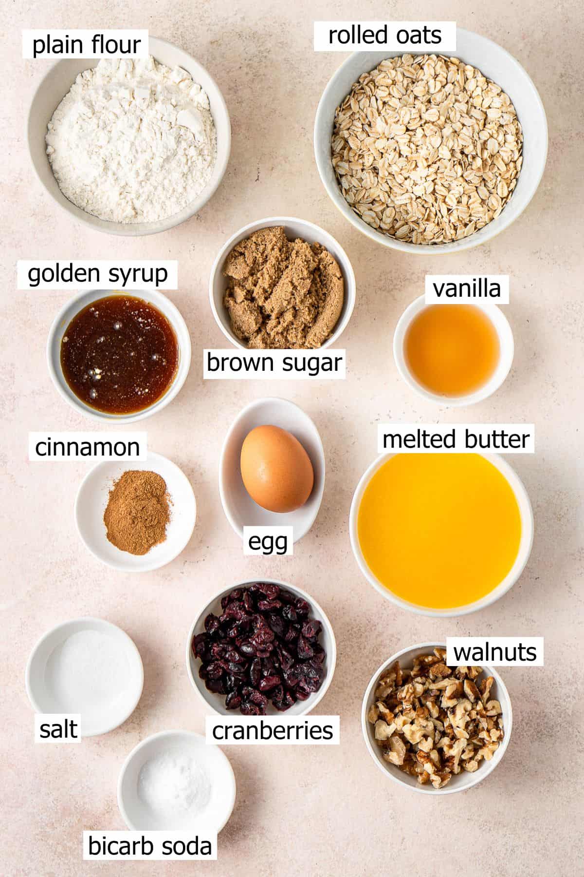 All ingredients needed to make oatmeal cranberry walnut cookies laid out in small bowls.