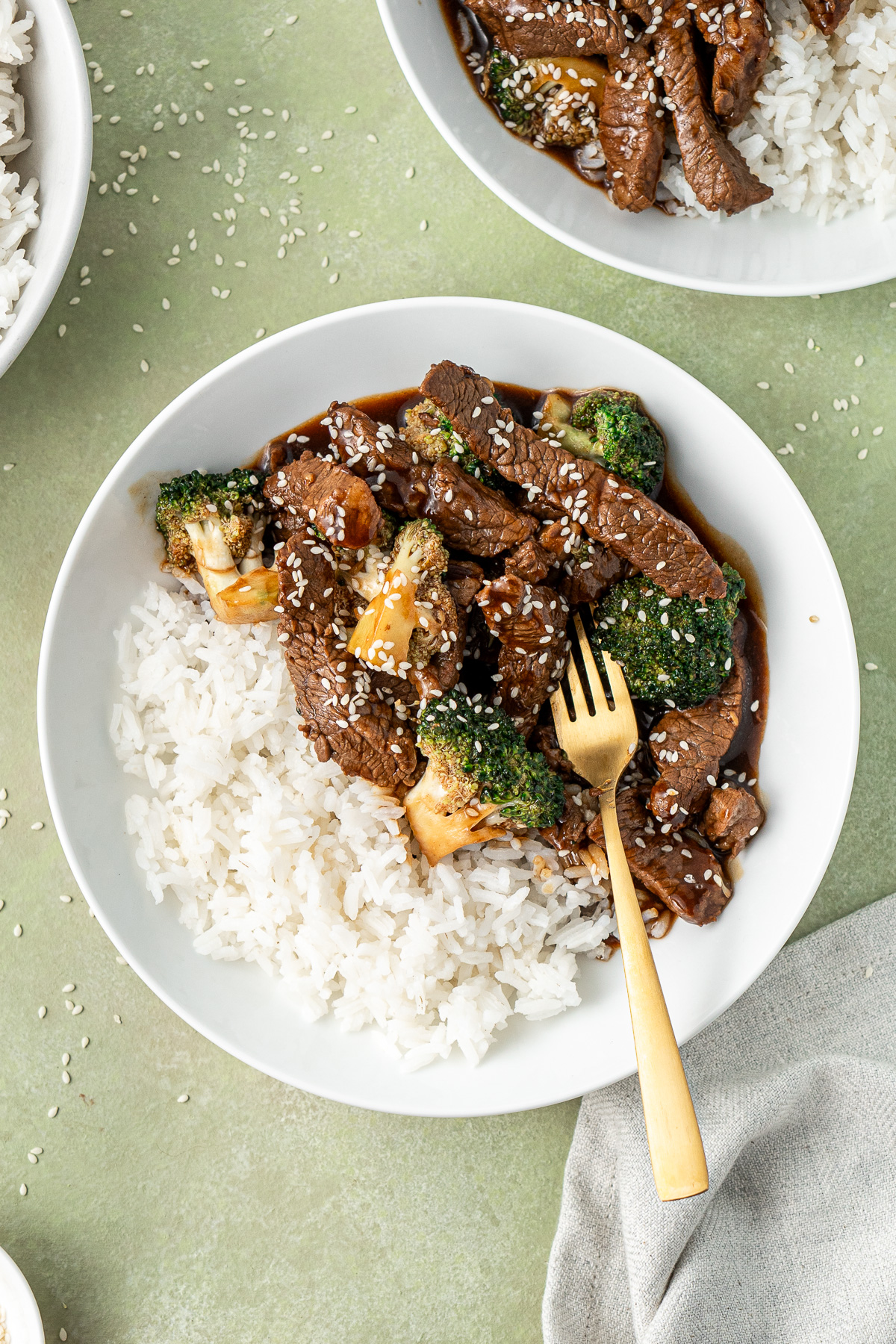 The beef and broccoli in a white bowl with a gold fork.