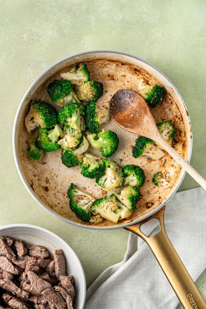 Cooking the broccoli in a frying pan with a wooden spoon.