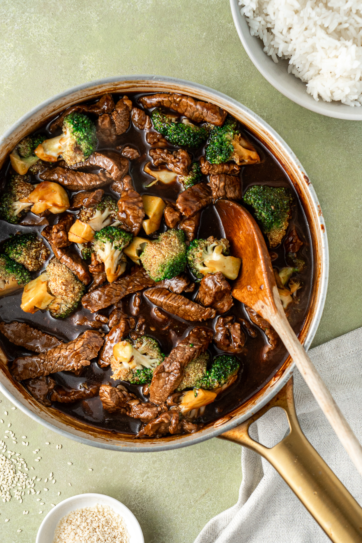 The beef and broccoli with the sauce in a frying pan with a wooden spoon.