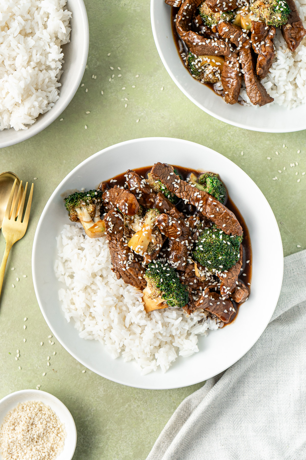 Beef and broccoli served into bowls with rice and topped with sesame seeds.