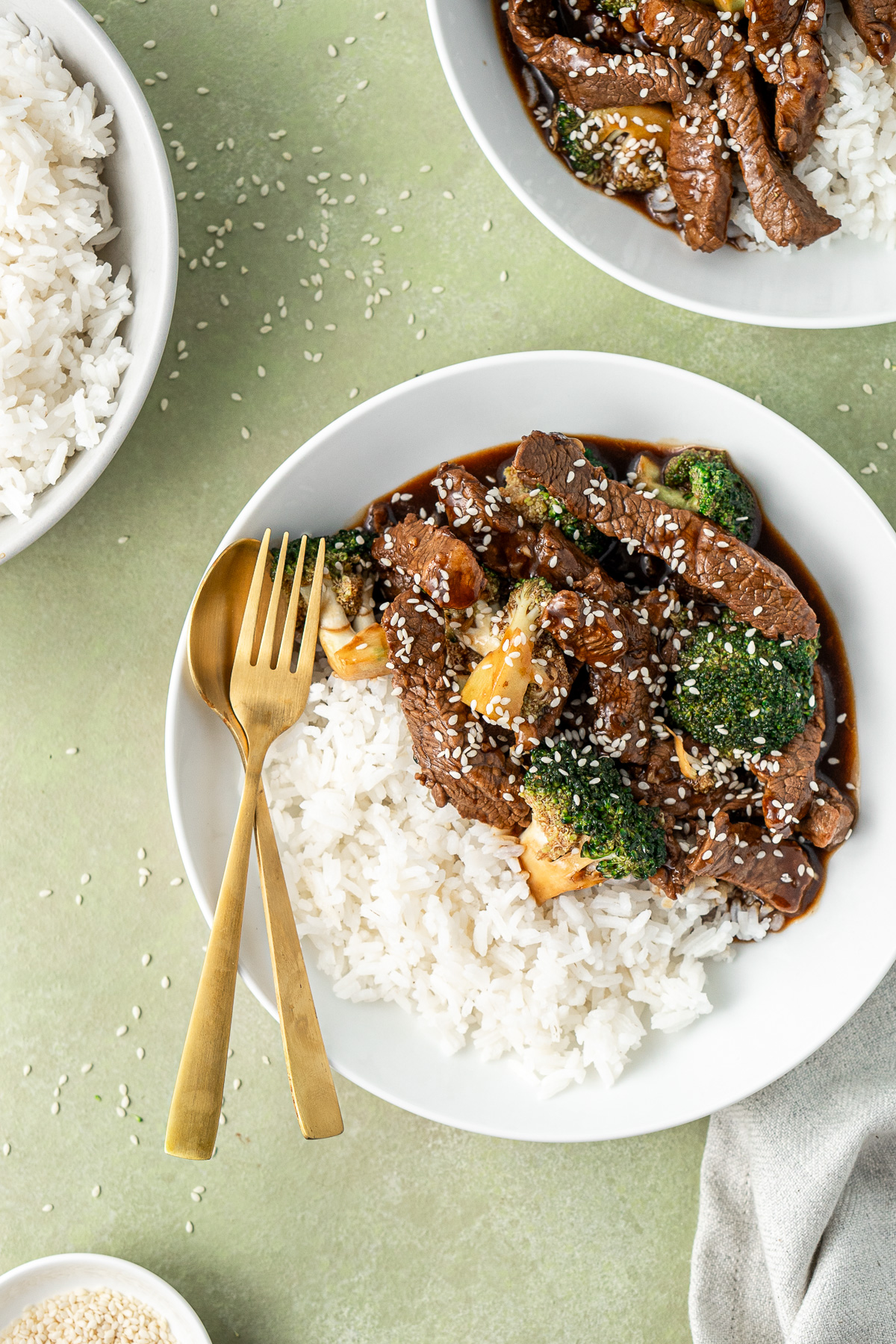 Close up of beef and broccoli over rice with gold cutlery.