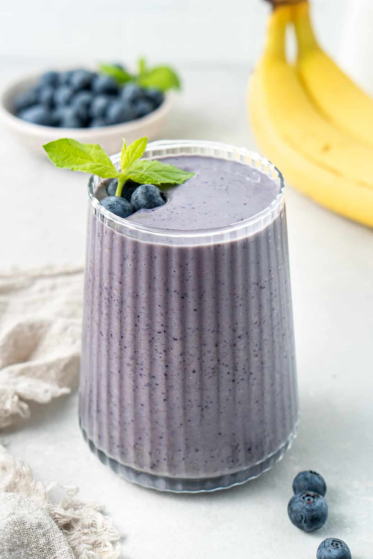 A blueberry banana smoothie in a glass topped with fresh blueberries and a sprig of mint. 