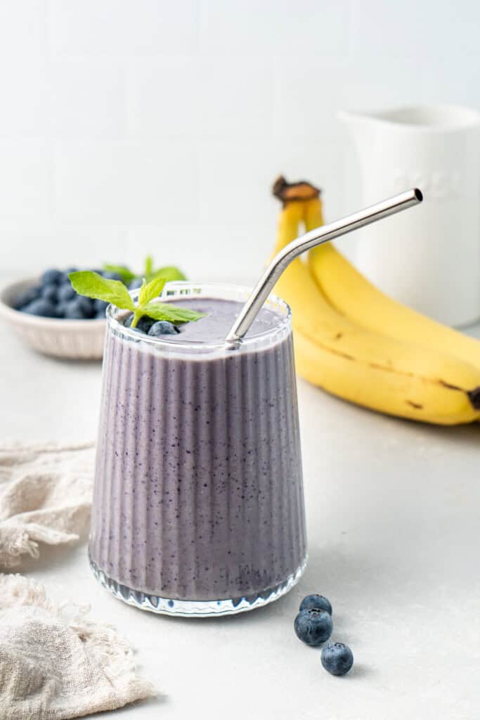 Blueberry banana smoothie in a glass with a straw.