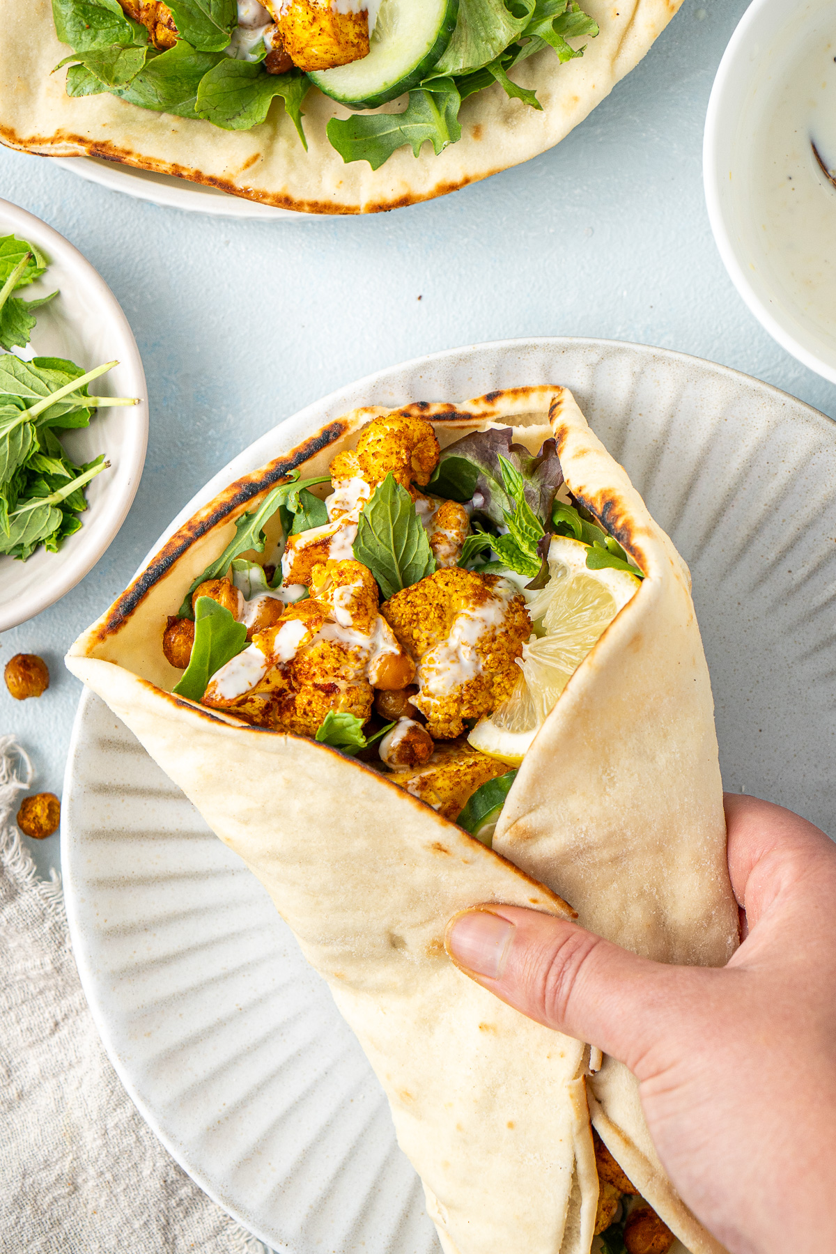 A hand wrapping up the cauliflower and chickpea shawarma in the pita bread on a plate.