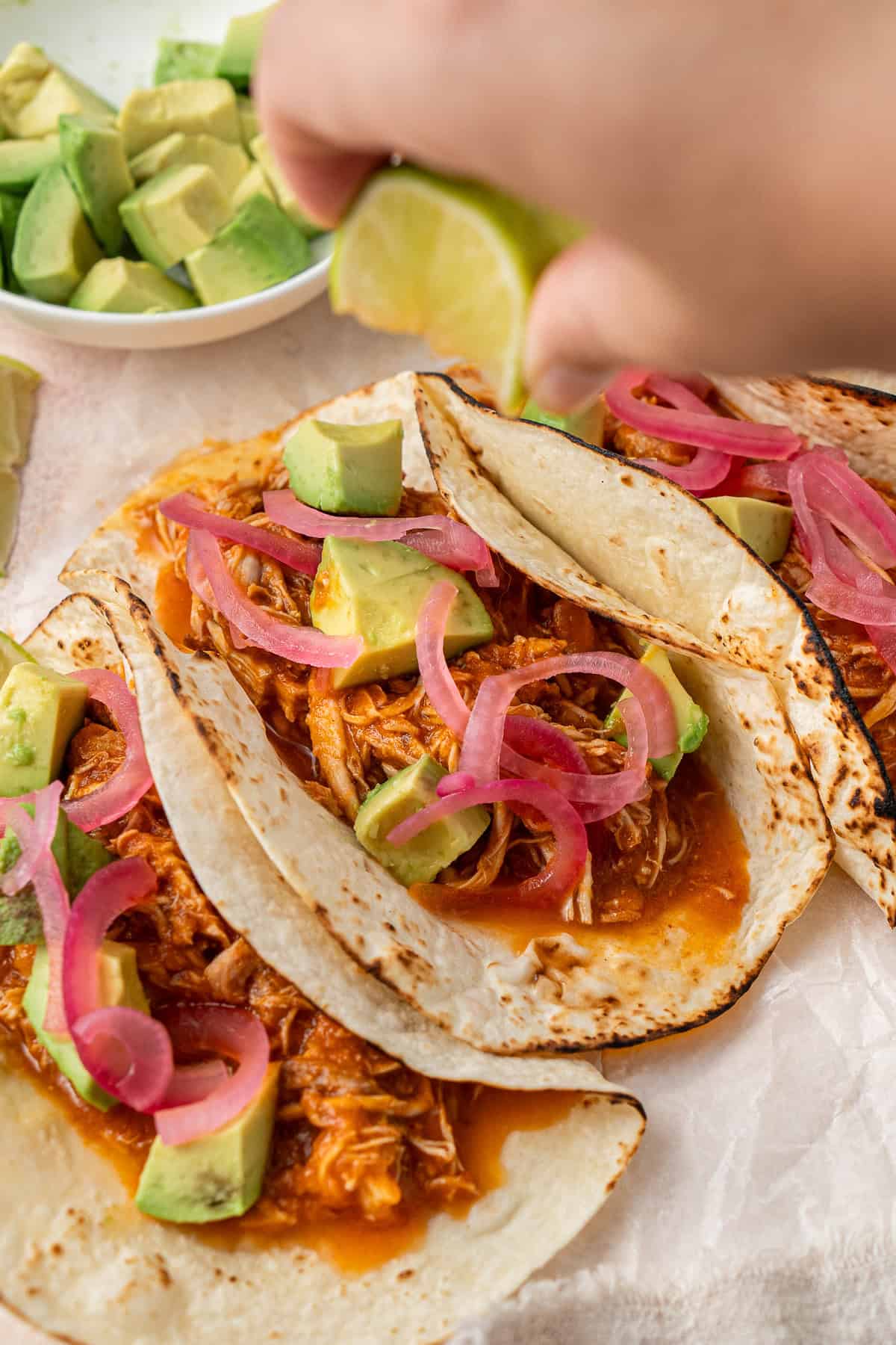 A hand squeezing lime over chicken tinga tacos.