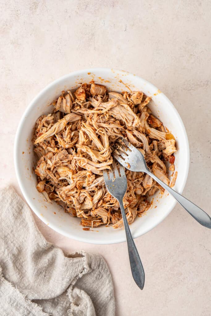 Shredding the chicken in a bowl with two forks.