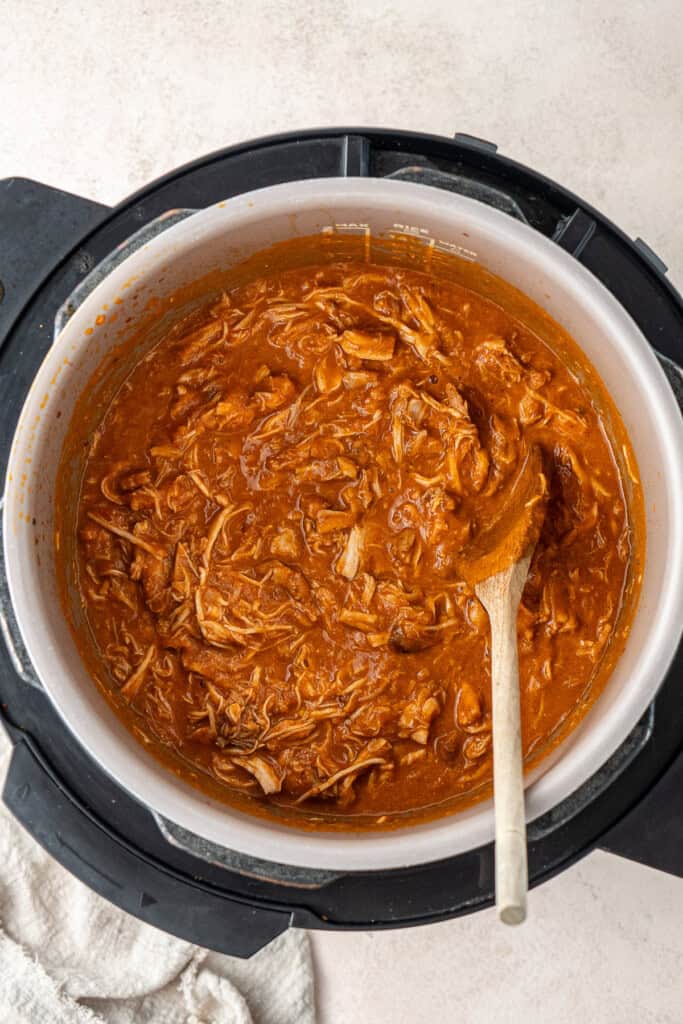 The chicken tinga in the slow cooker with a wooden spoon.