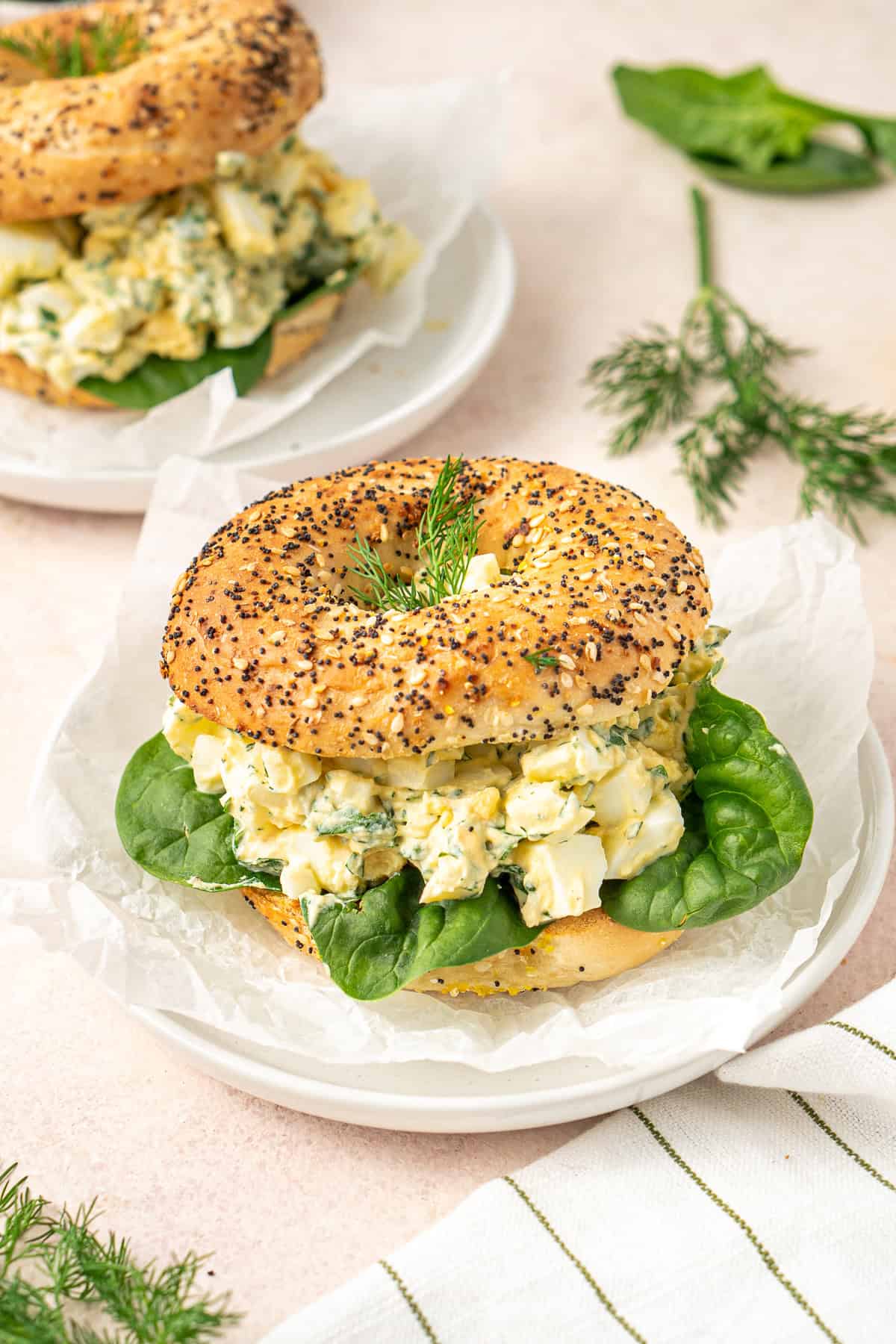 Egg salad bagel with baby spinach on a plate. 