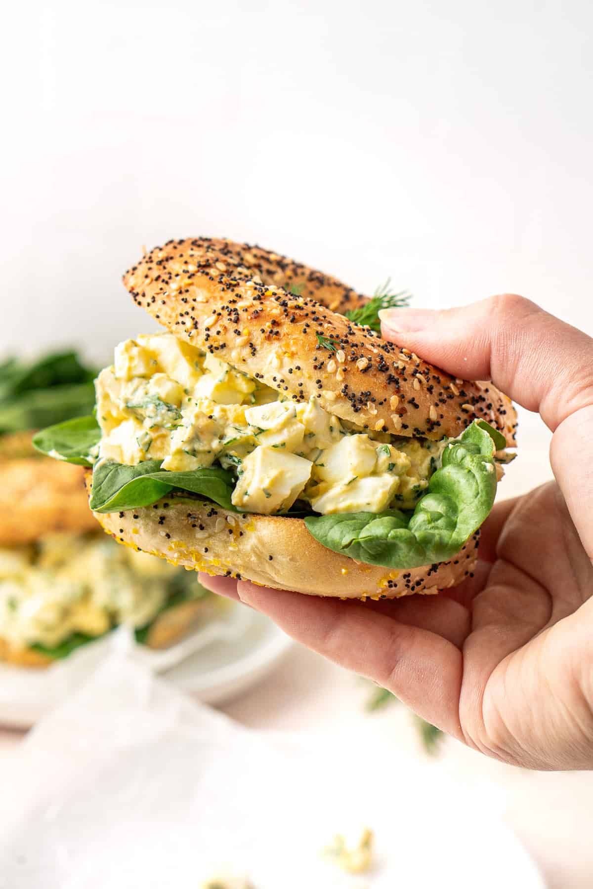 A hand holding an egg salad bagel sandwich. 