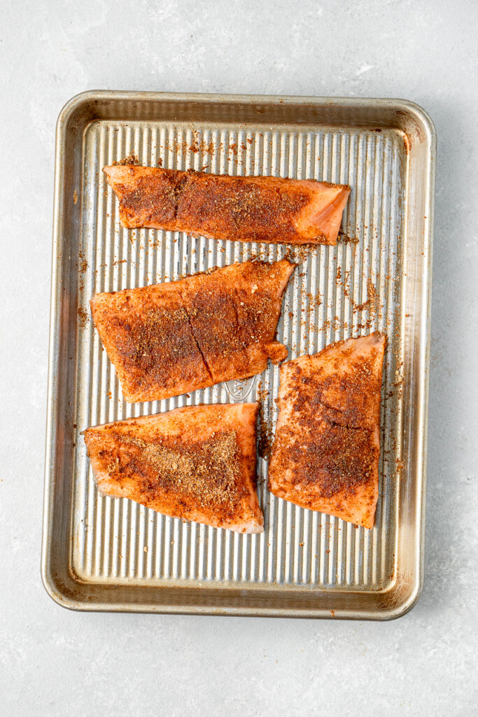 The salmon fillets coated in the spice mixture on a baking tray.