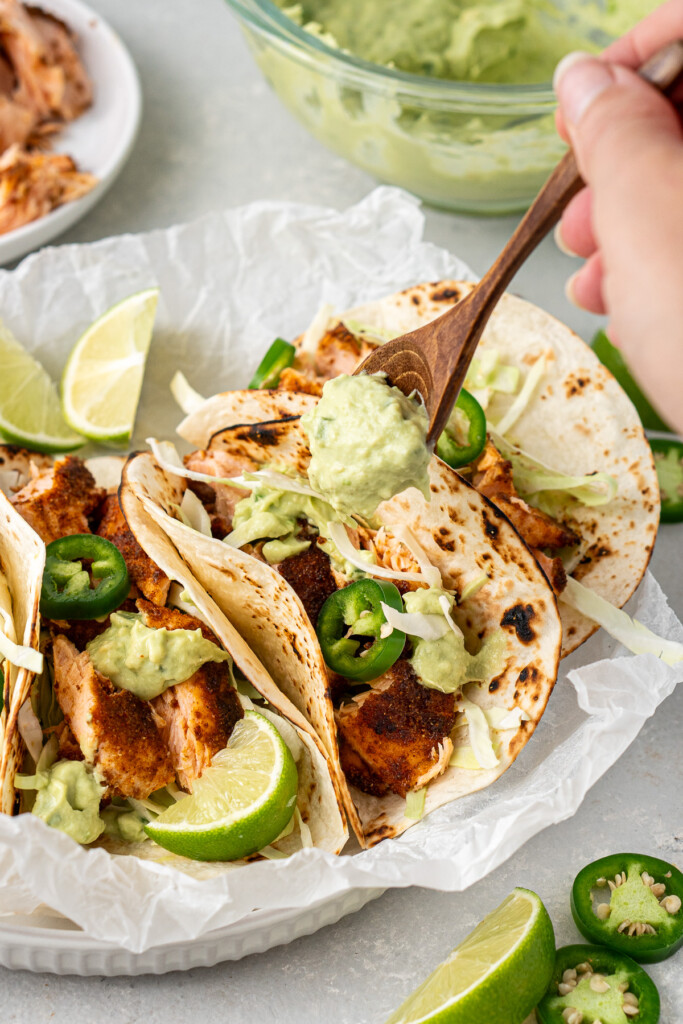 Spooning the avocado crema over the assembled tacos.