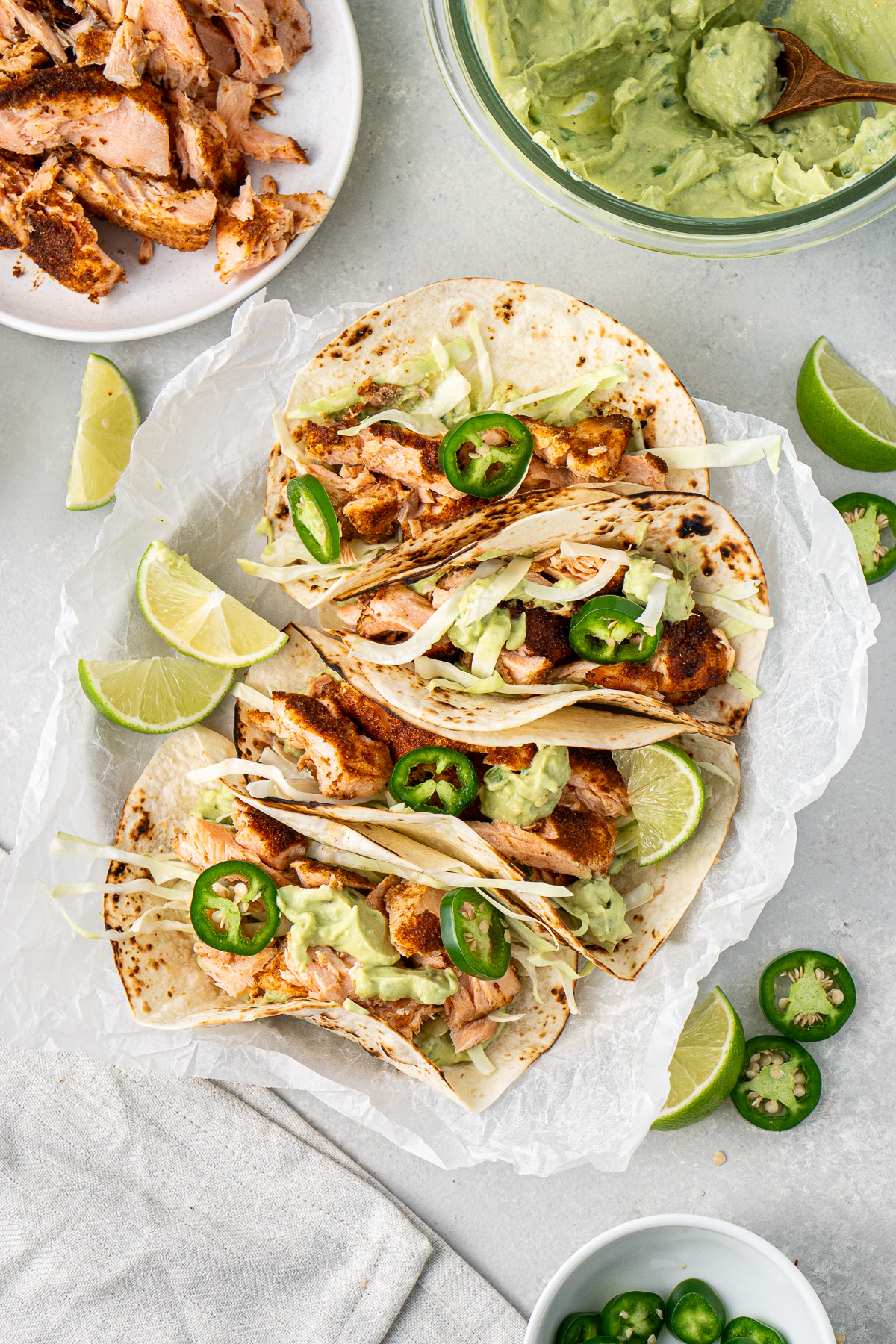 Four grilled salmon tacos on a plate served with lime and fresh jalapenos. 