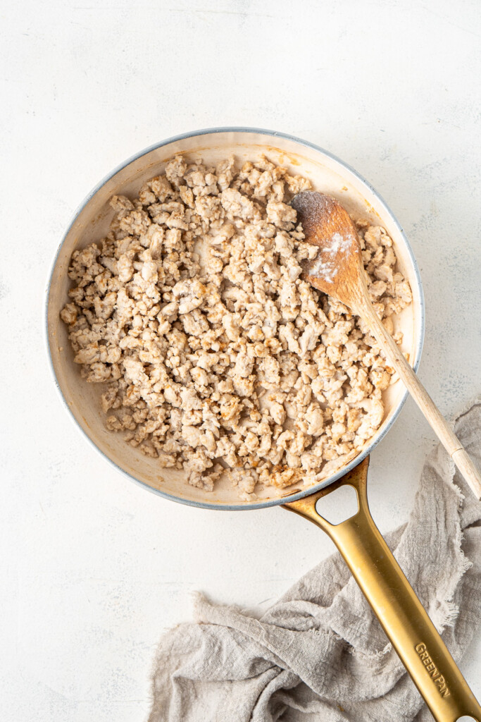 Browning chicken mince in a frying pan with a wooden spoon.