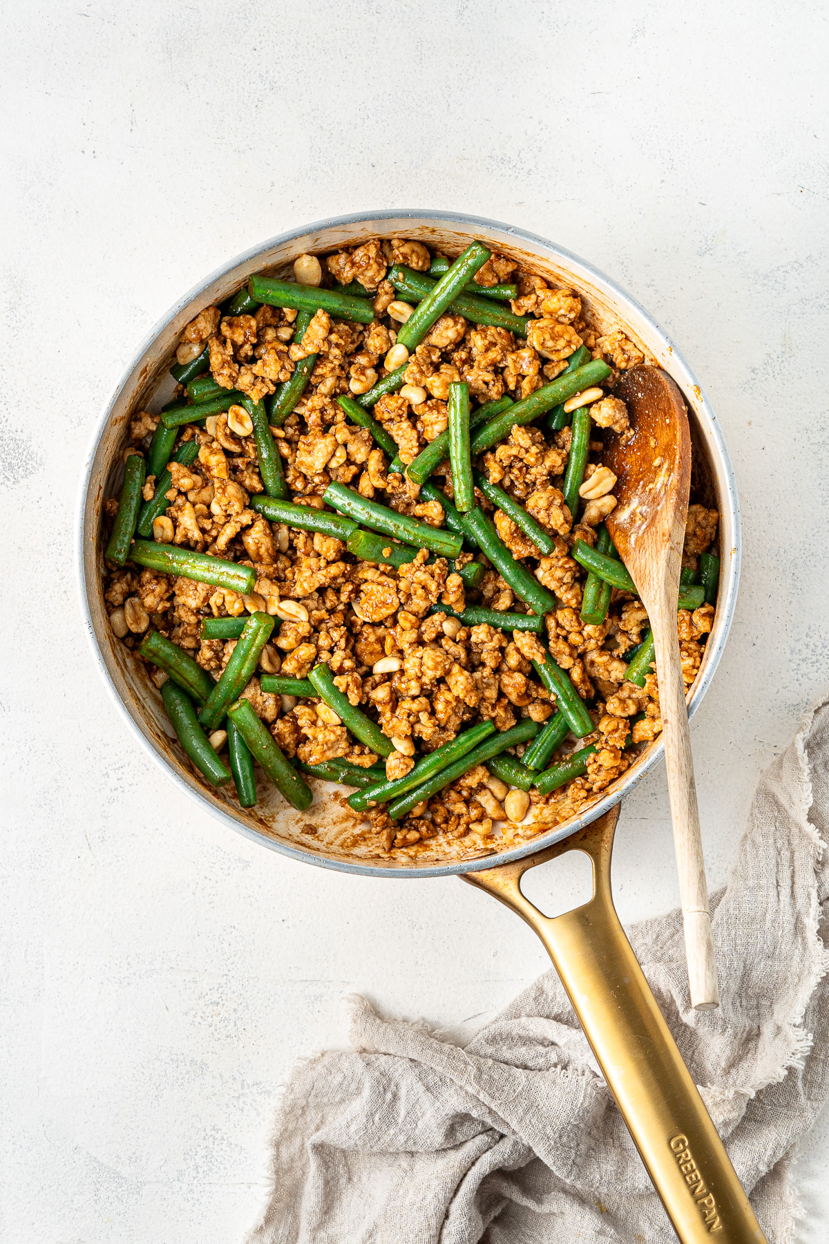 Hoisin chicken and beans with sauce in a frying pan with a wooden spoon.