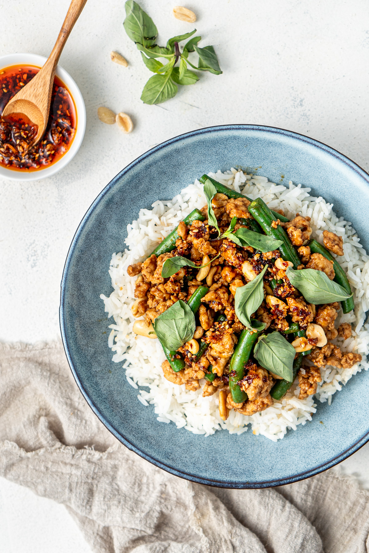 Close up of hoisin chicken stir fry in a blue bowl, over rice with Thai basil.