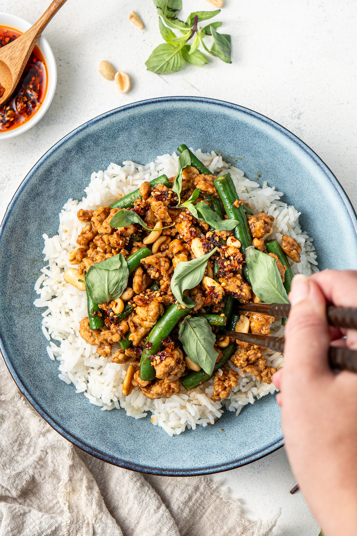 A hand using chopsticks to take a bite of hoisin chicken stir fry and rice.