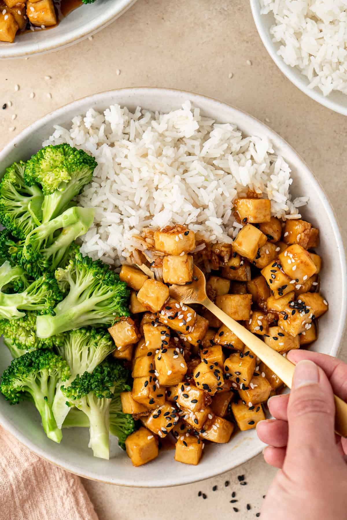 Close up of a hand taking a bite of the honey garlic tofu with rice and broccoli.