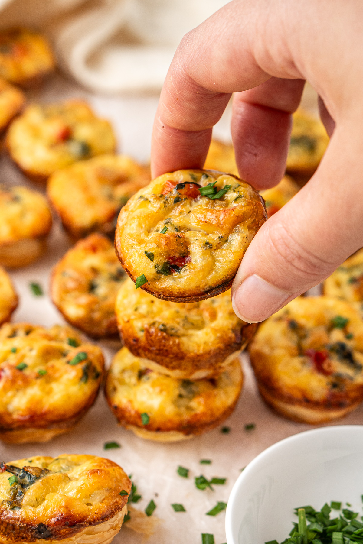 A hand picking up a mini vegetable quiche.