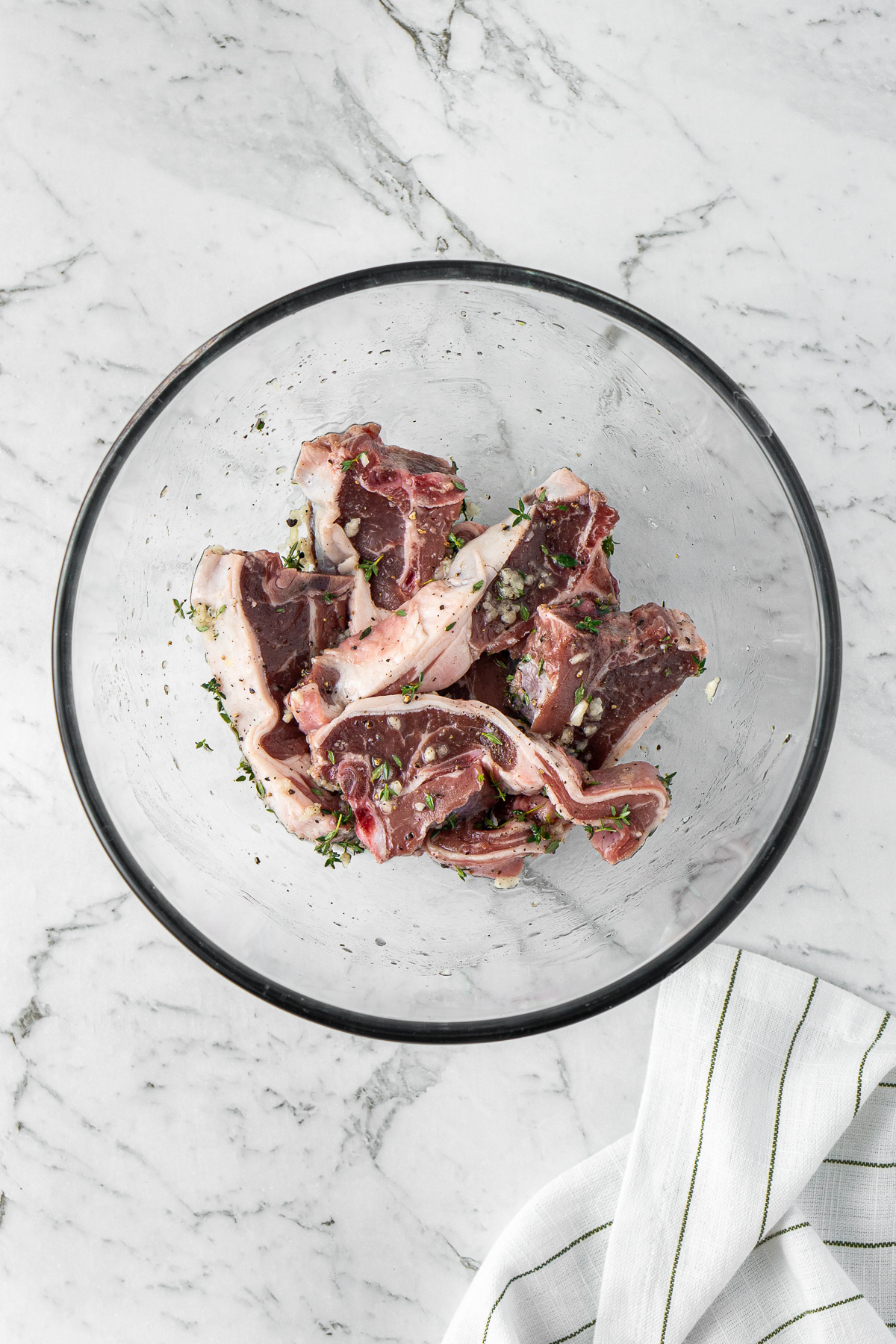 Lamb chops marinating in a bowl with herbs and garlic.