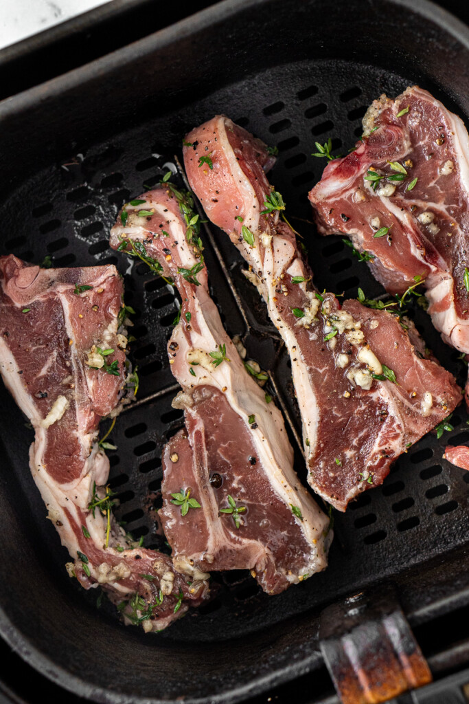 Raw lamb chops in the basket of the air fryer.