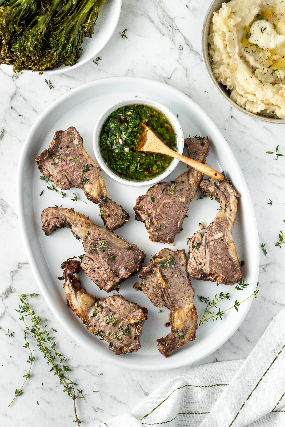 Cooked lamb chops in a plate with a side of chimichurri sauce.