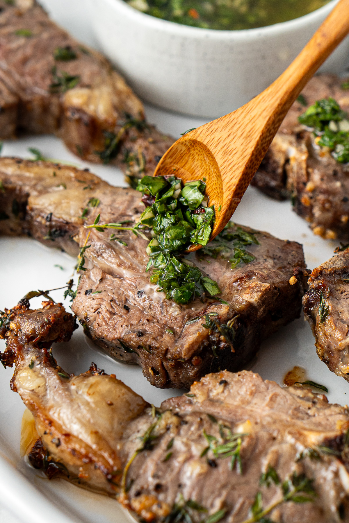 Close up of a spoon adding chimichurri to a perfectly cooked lamb chop.