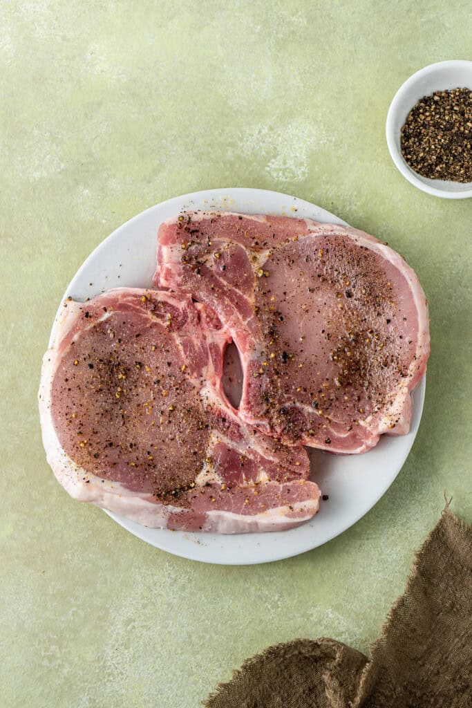 Seasoning the raw bone in pork chops with salt and pepper. 