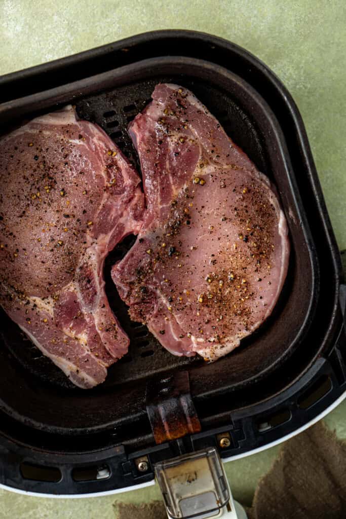 Raw pork chops in the basket of the air fryer. 