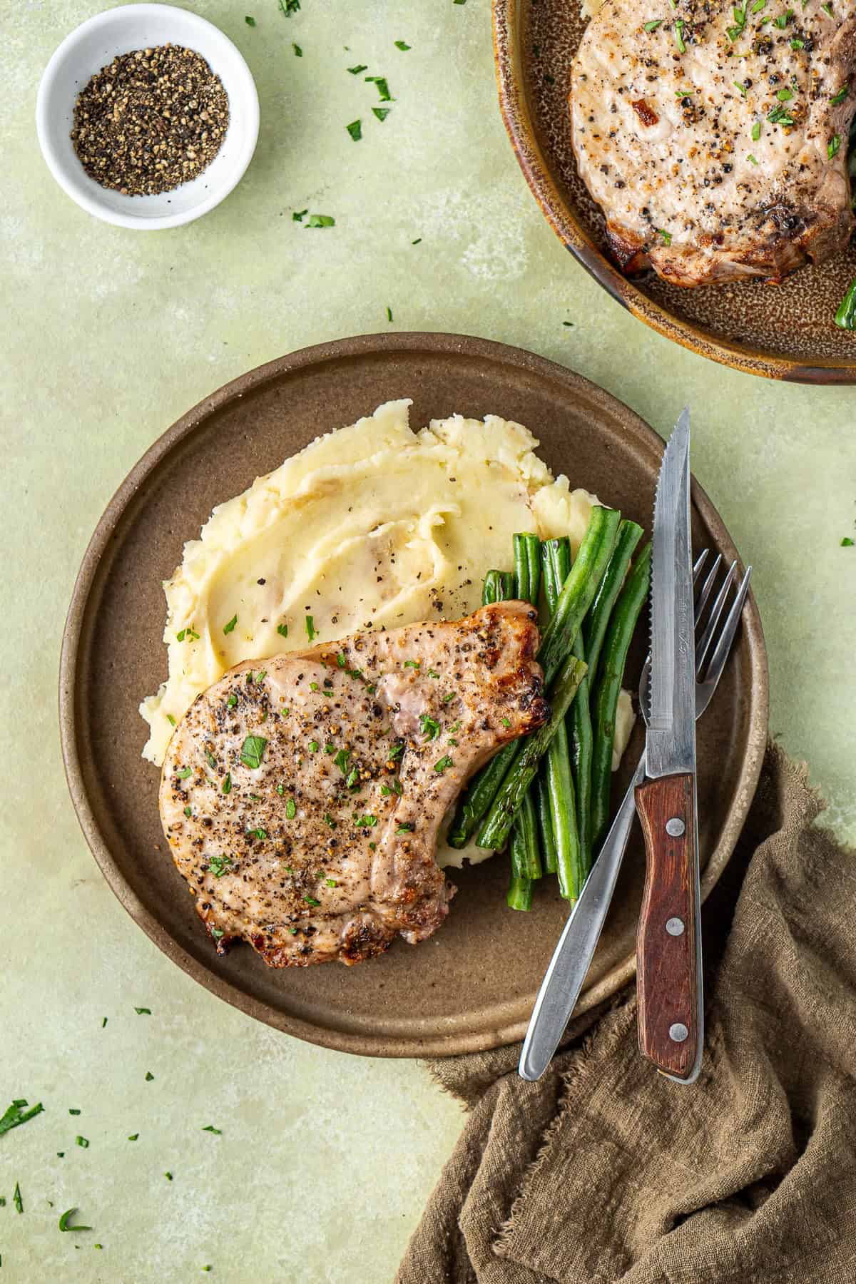 Air fryer pork chop served on a plate with mashed potatoes and green beans. 