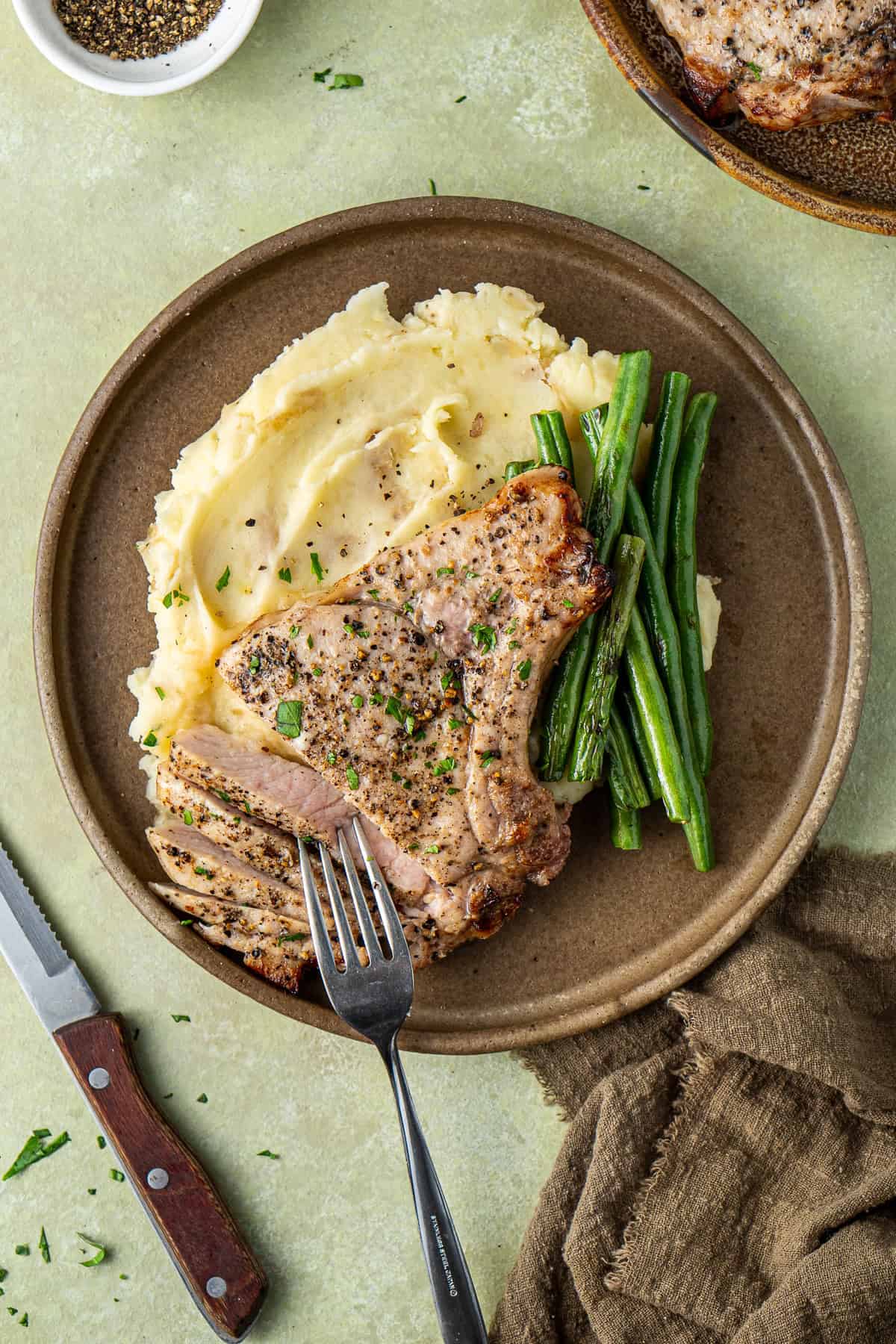 A fork taking a piece of sliced pork chop from the plate. 