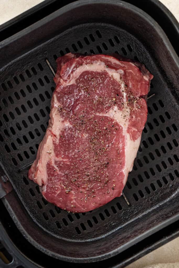 A raw steak in the basket of an air fryer.