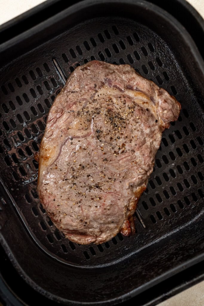 The cooked steak in the basket of the air fryer.