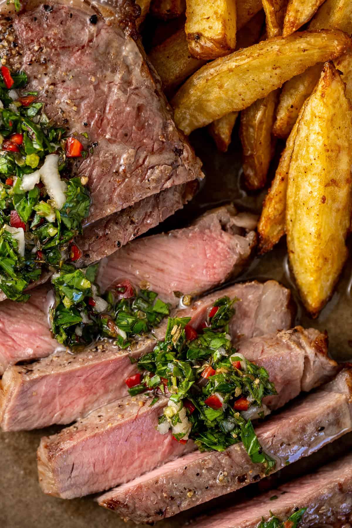 Close up of sliced cooked steak with chimichurri.