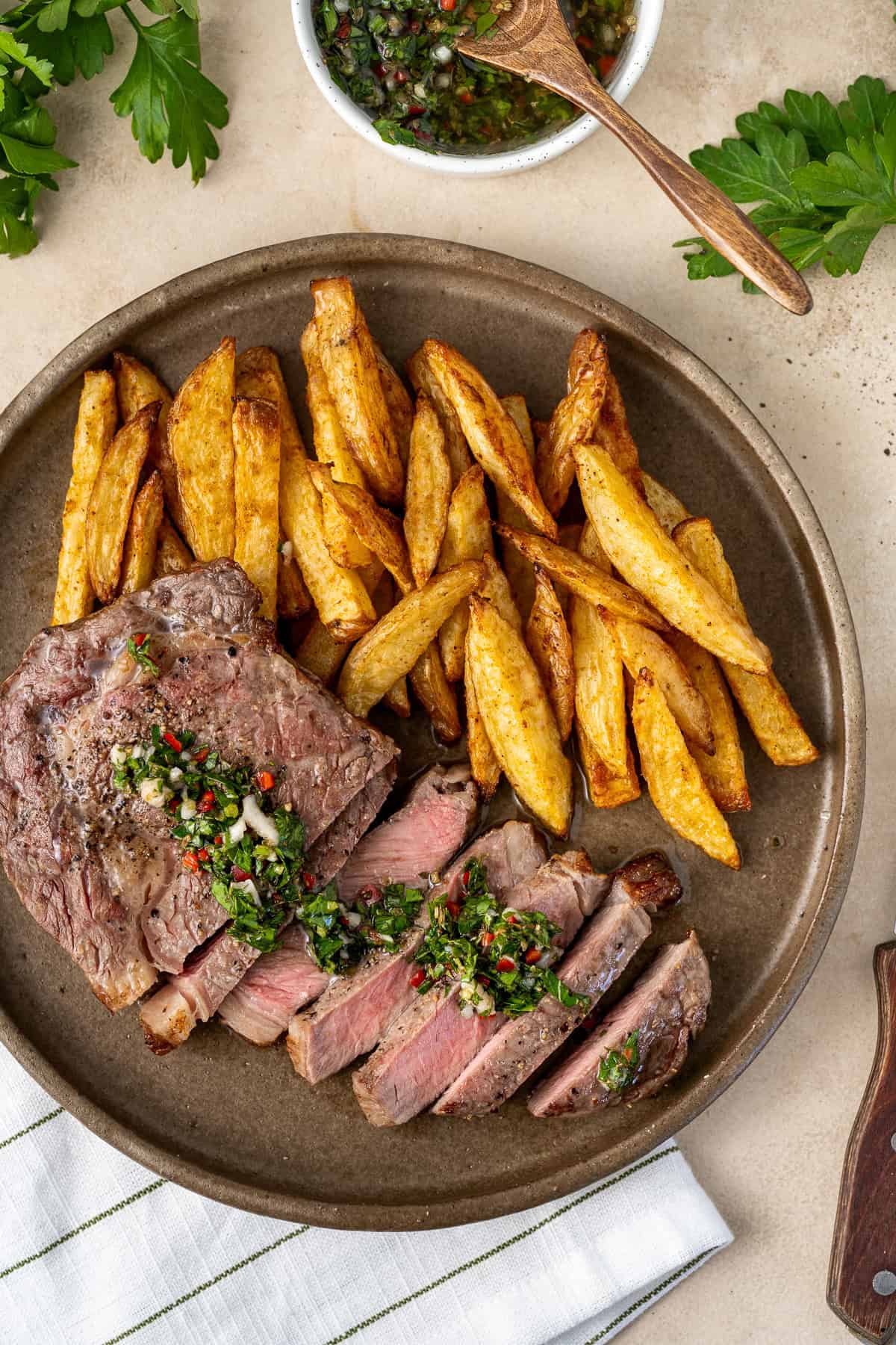 Sliced, medium-rare air fryer steak served on a plate with chimichurri and oven baked fries. 