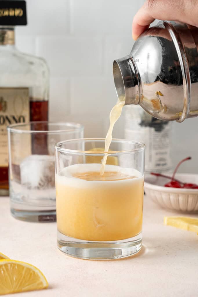 Straining the amaretto sour cocktail into a glass.