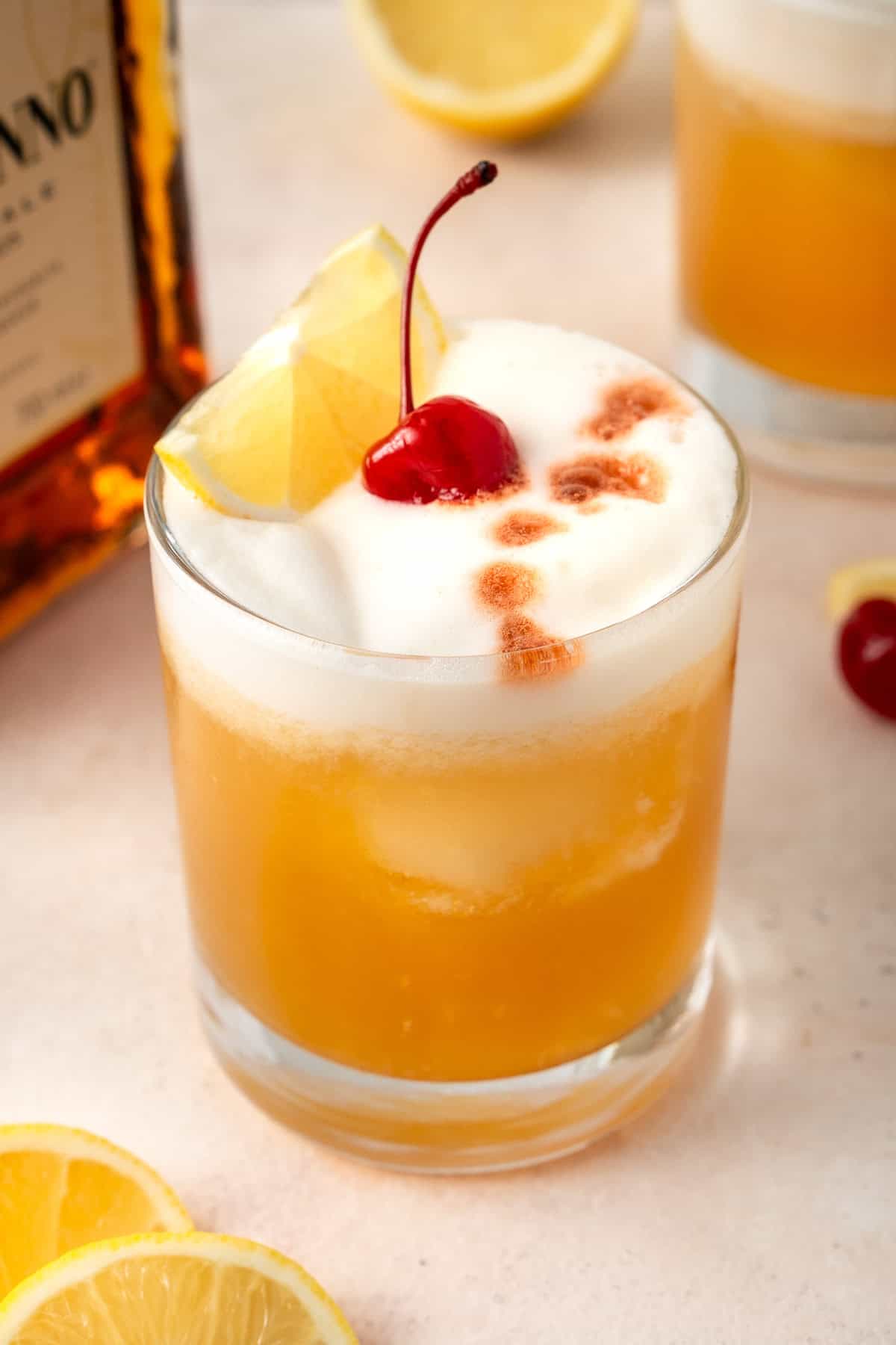 Close up of an amaretto sour with bitters and a cherry.